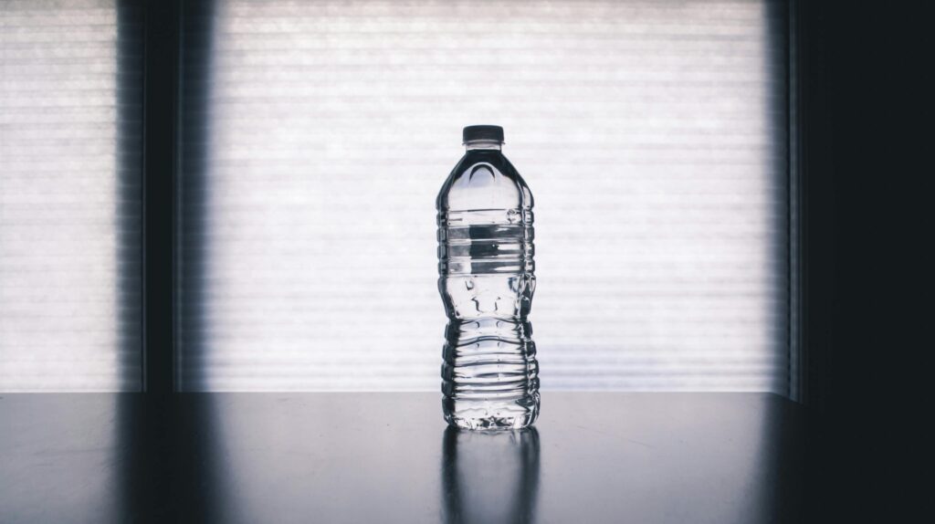 Stylish photo of a clear plastic water bottle on a reflective surface with a soft shadow.