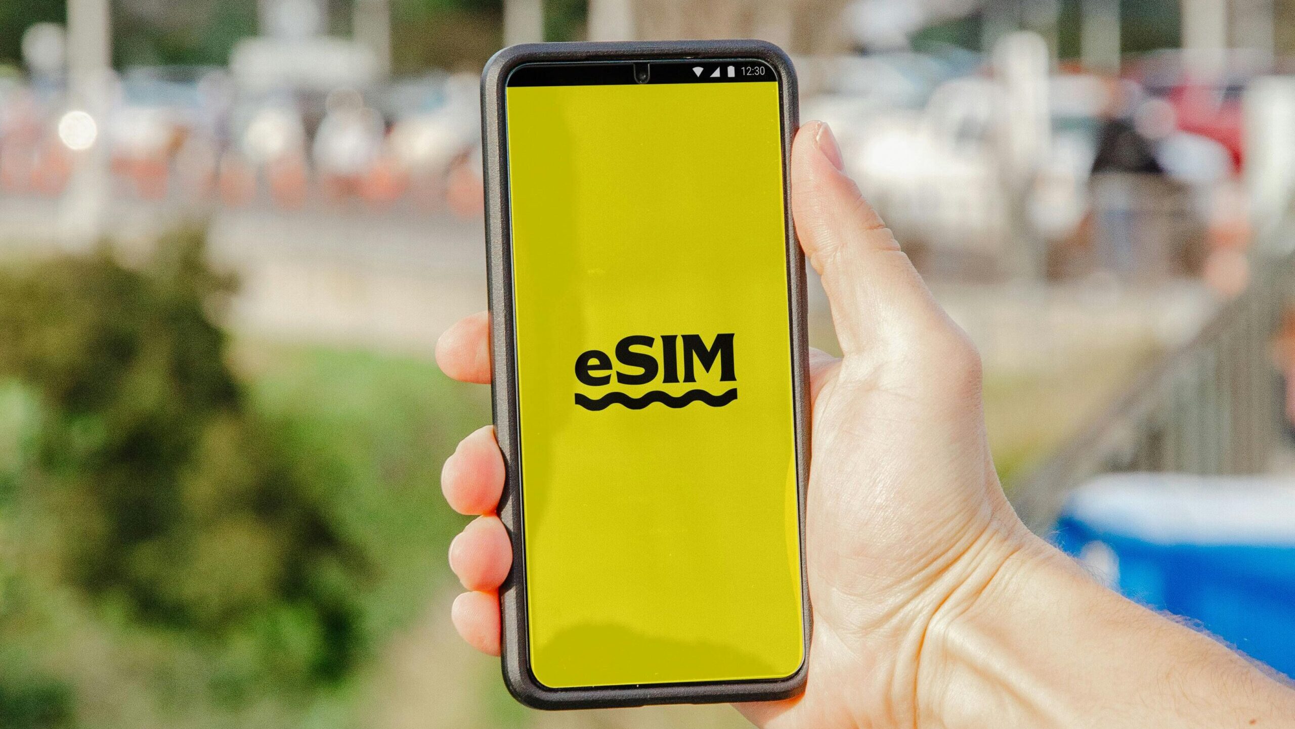 A person holds a smartphone featuring an eSIM display against an outdoor urban backdrop.